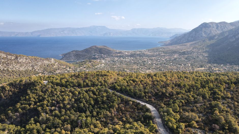 A breathtaking aerial view of a coastal village with lush greenery and mountains meeting the sea under daylight.